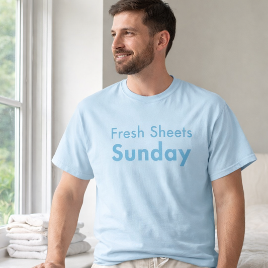 Man wearing chambray Fresh Sheets Sunday Comfort Colors T-shirt standing beside bright window in airy bedroom
