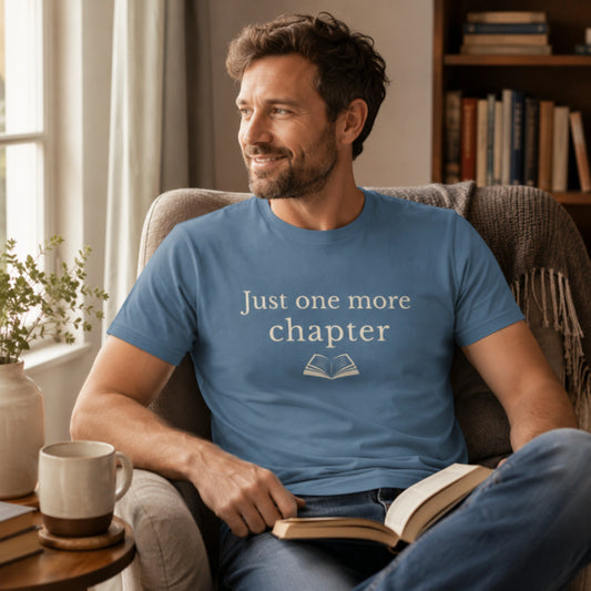 Male model wearing the Steel Blue “Just One More Chapter” T-Shirt while relaxing in a cosy armchair with a book and mug in a calm reading corner.