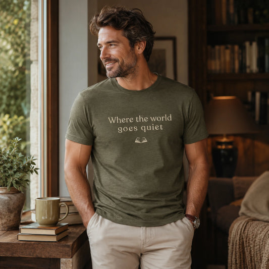 Man wearing the Heather Olive “Where the World Goes Quiet” T-Shirt, standing in a calm, book-lined interior with soft natural light and a relaxed, thoughtful feel.
