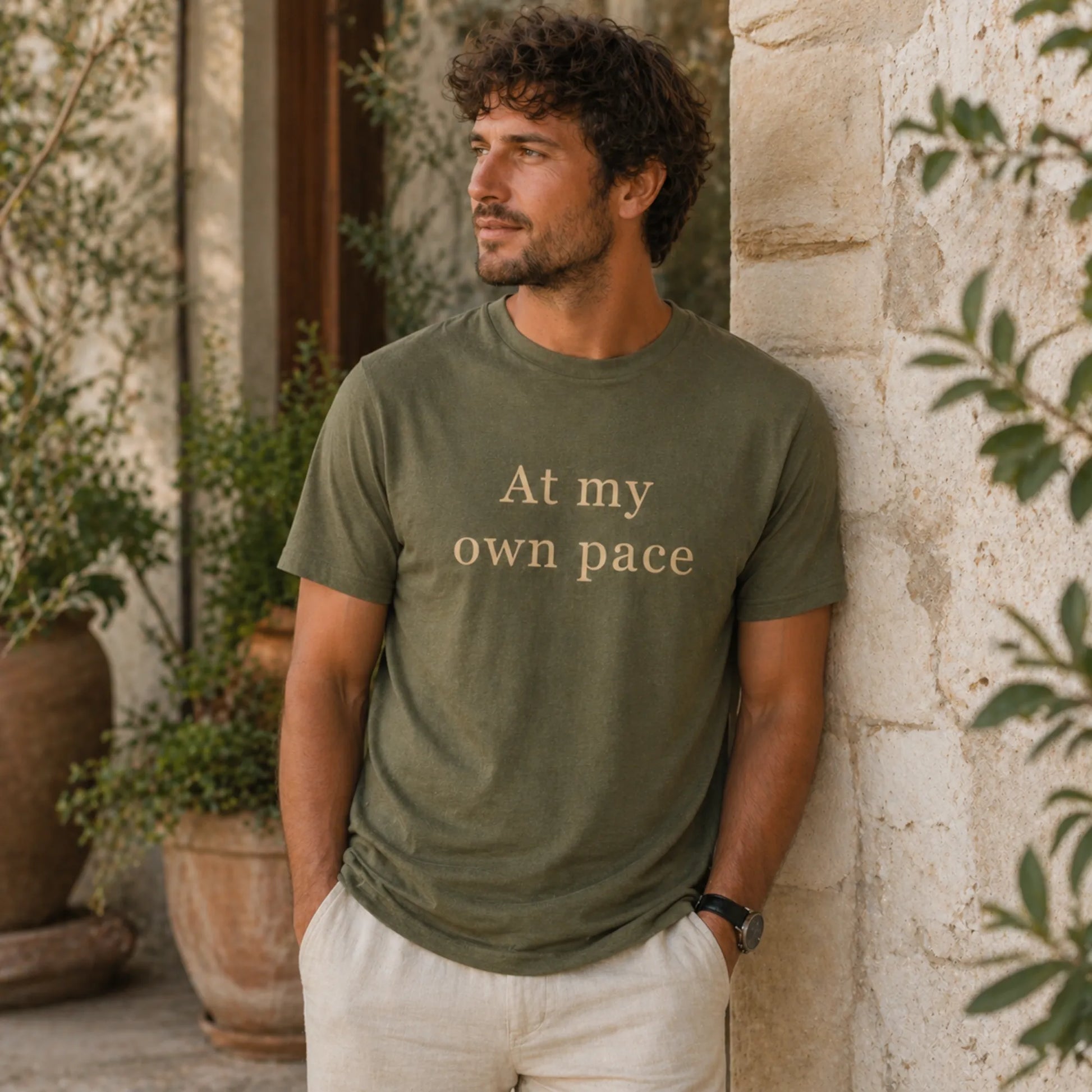 Male model wearing an At My Own Pace T-Shirt in heather olive in a warm, relaxed lifestyle setting.