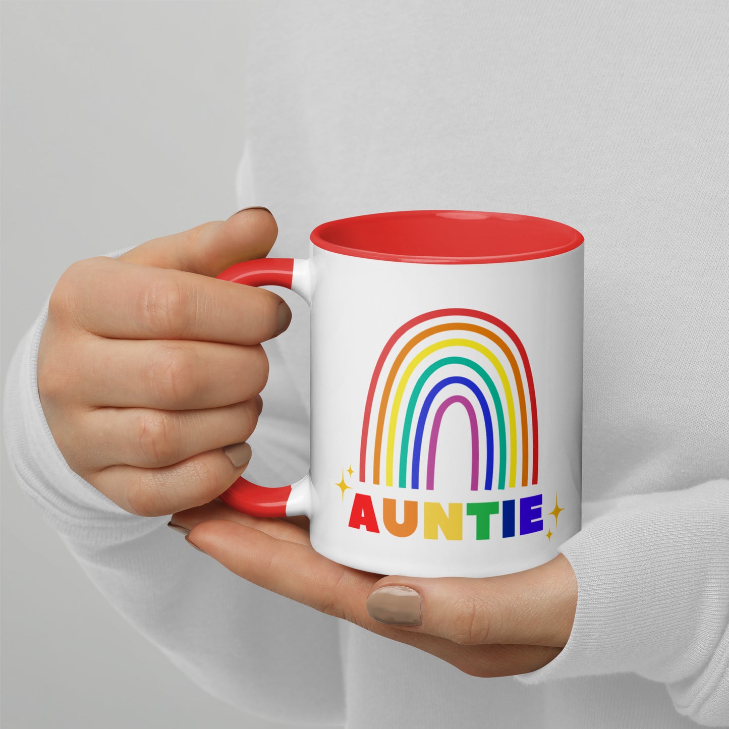 Hand holding Auntie rainbow ceramic mug with red interior visible