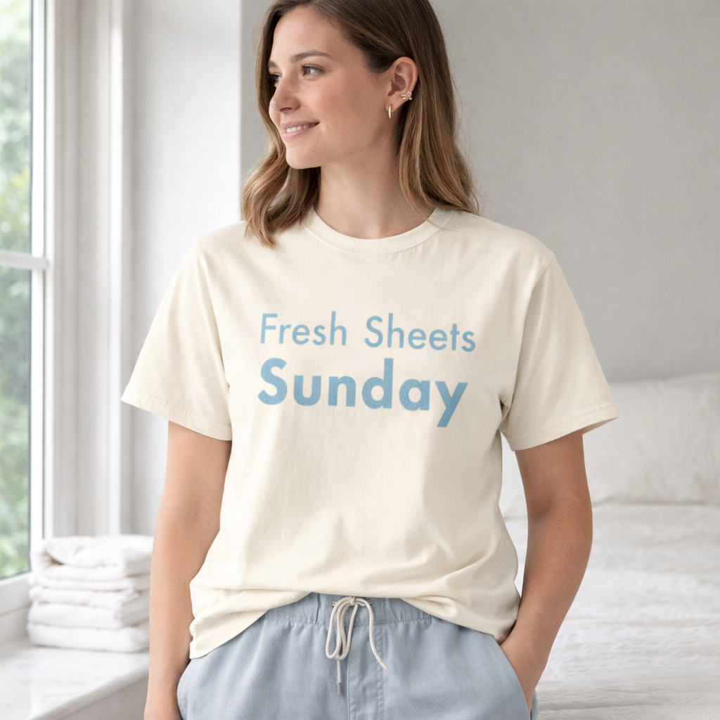 Woman wearing ivory Fresh Sheets Sunday Comfort Colors T-shirt in calm bedroom with soft morning light