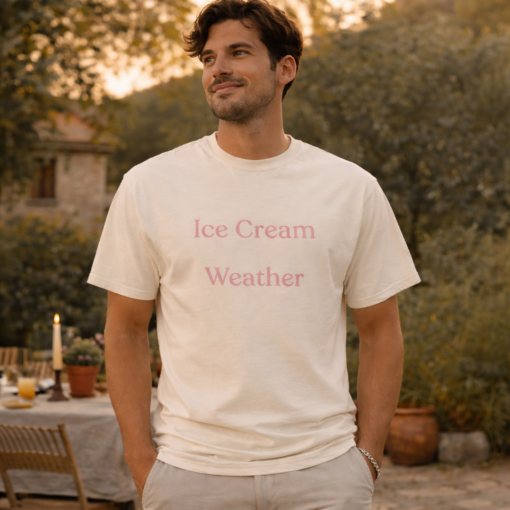 Ice Cream Weather slogan T-shirt in ivory with soft pink lettering worn by a man outdoors during golden hour, relaxed summer lifestyle mockup
