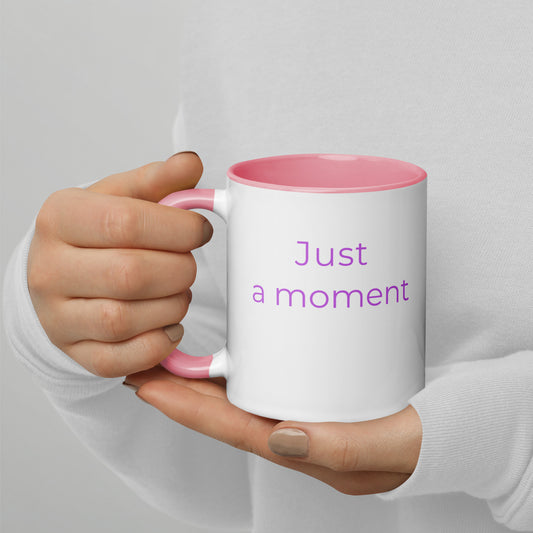 Ceramic coffee mug with pink handle and the words “just a moment”, held in hands with soft knit sleeves, capturing a calm and reflective pause.