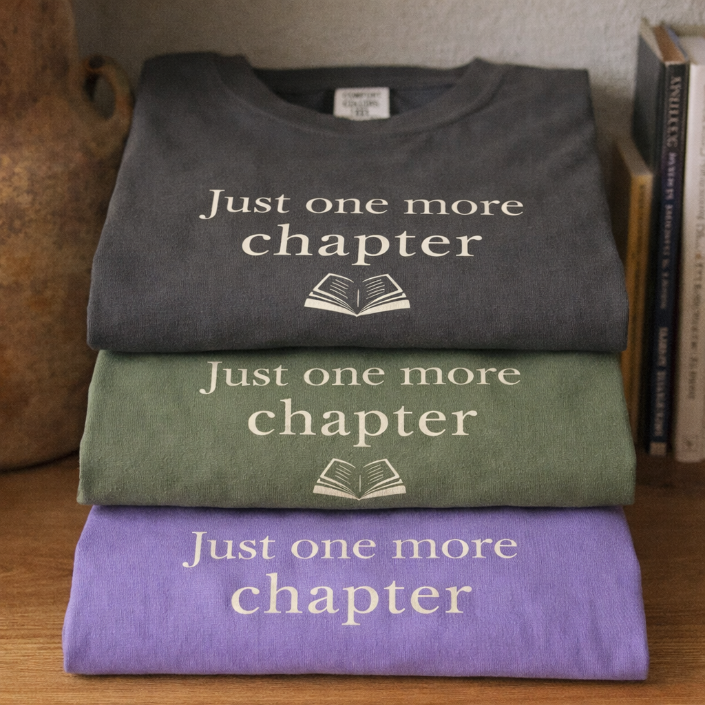 Folded stack of Comfort Colors T-shirts in Pepper Moss and Violet with Just one more chapter design