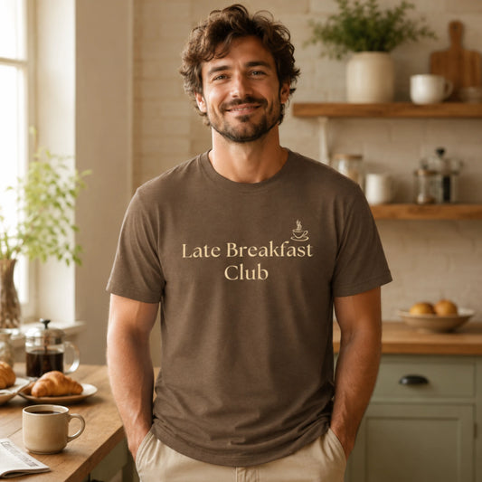 Male model wearing a heather brown Late Breakfast Club T-shirt with soft cream text in a cosy morning kitchen setting.
