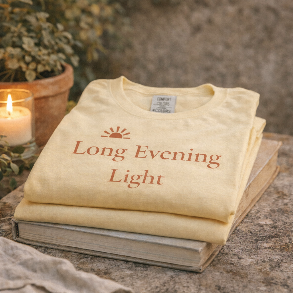 Folded Long Evening Light butter T-shirt stacked on books with candle and terracotta pot