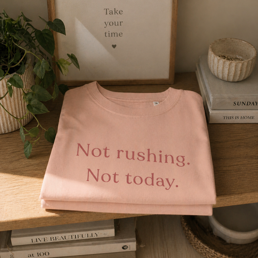 Folded Not Rushing Not Today T-shirt on wooden shelf with books and plant, soft neutral home setting