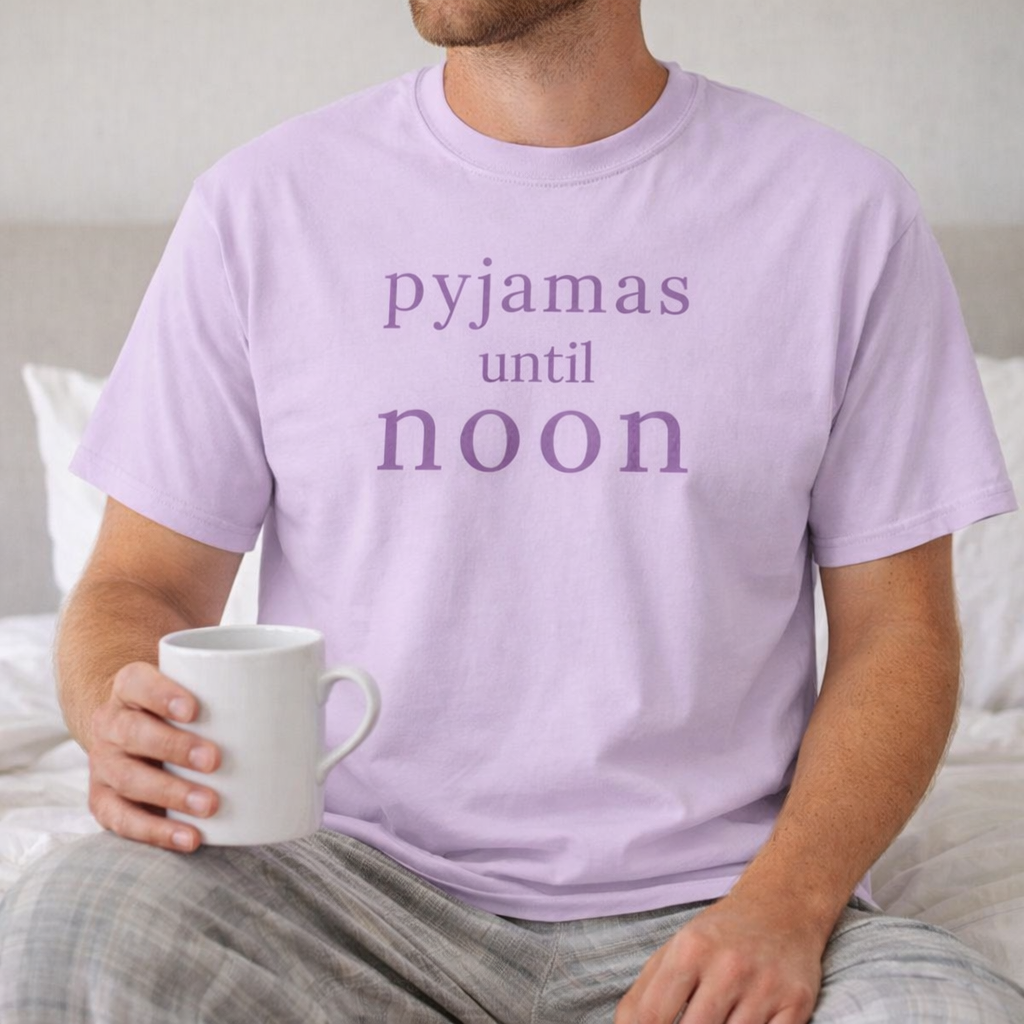 Man relaxing in bed wearing orchid Pyjamas Until Noon Comfort Colors T-shirt holding a mug in a cosy bedroom setting