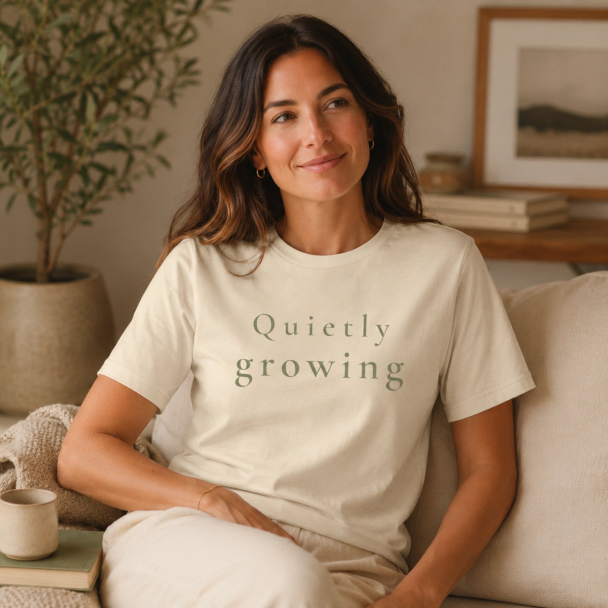 Female model wearing a Heather Natural Quietly Growing T-shirt in a calm, cosy indoor lifestyle setting.