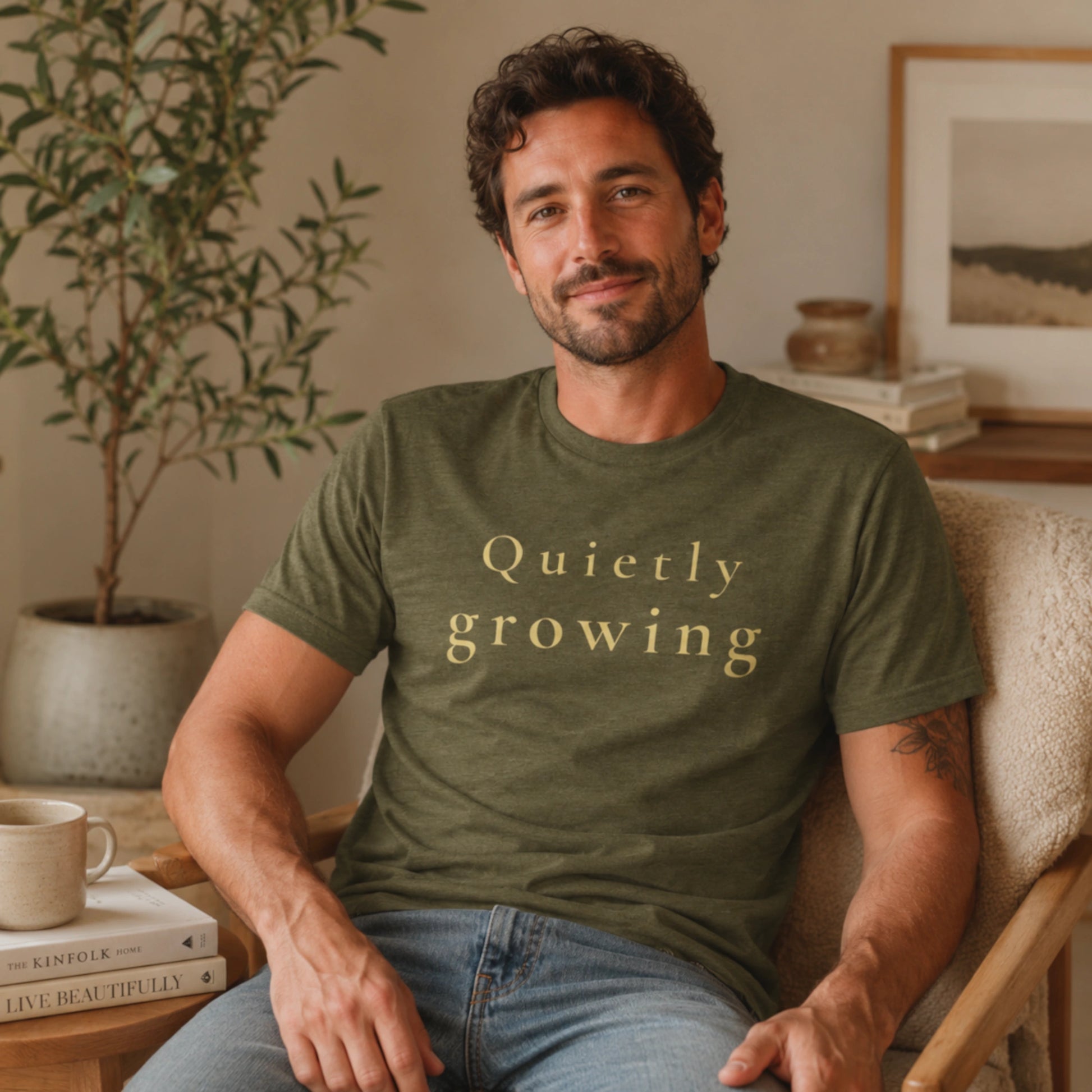Male model wearing a Heather Olive Quietly Growing T-shirt in a warm, softly lit indoor lifestyle setting.