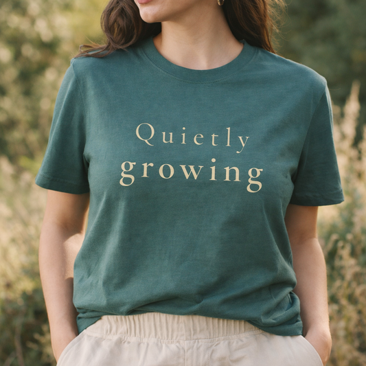 female model wearing blue spruce Comfort Colors T-shirt with “Quietly growing” text, soft lifestyle image with calm neutral tones