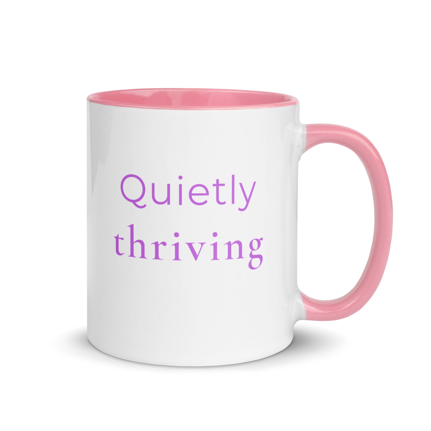 Minimalist ceramic coffee mug with pink handle and the phrase “quietly thriving”, designed for calm confidence and everyday positive moments.