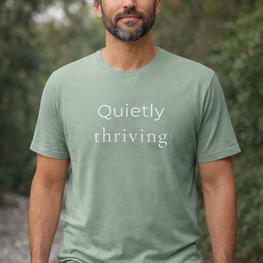 male model wearing sage green Bella Canvas T-shirt with “Quietly thriving” text, relaxed outdoor lifestyle image with soft natural light