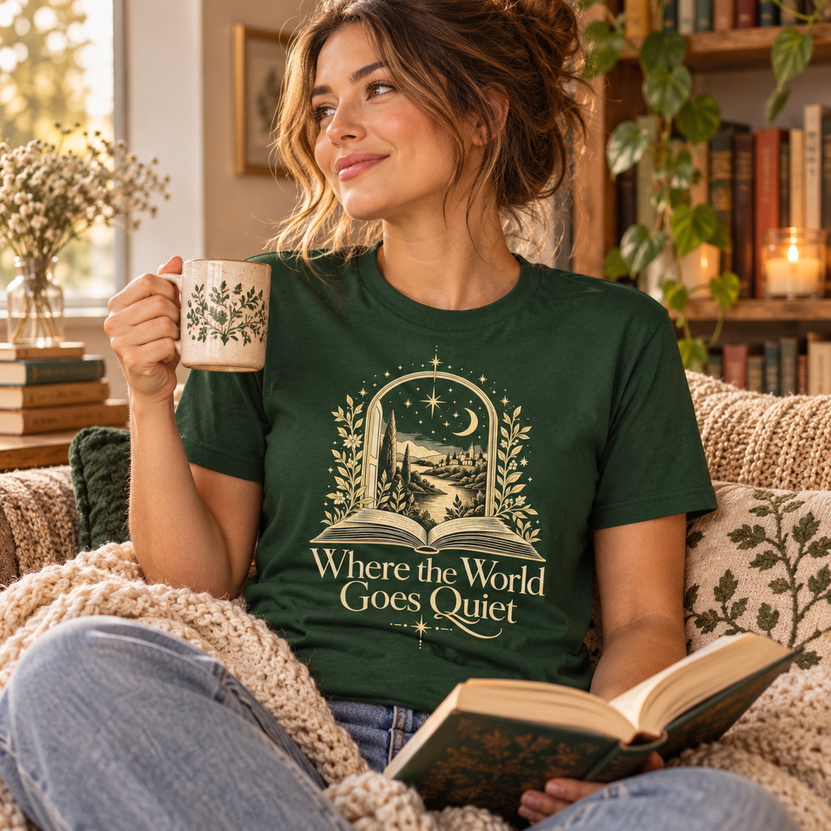 Woman wearing a green “Where the World Goes Quiet” illustrated T-shirt while relaxing in a warm, cosy reading setting.
